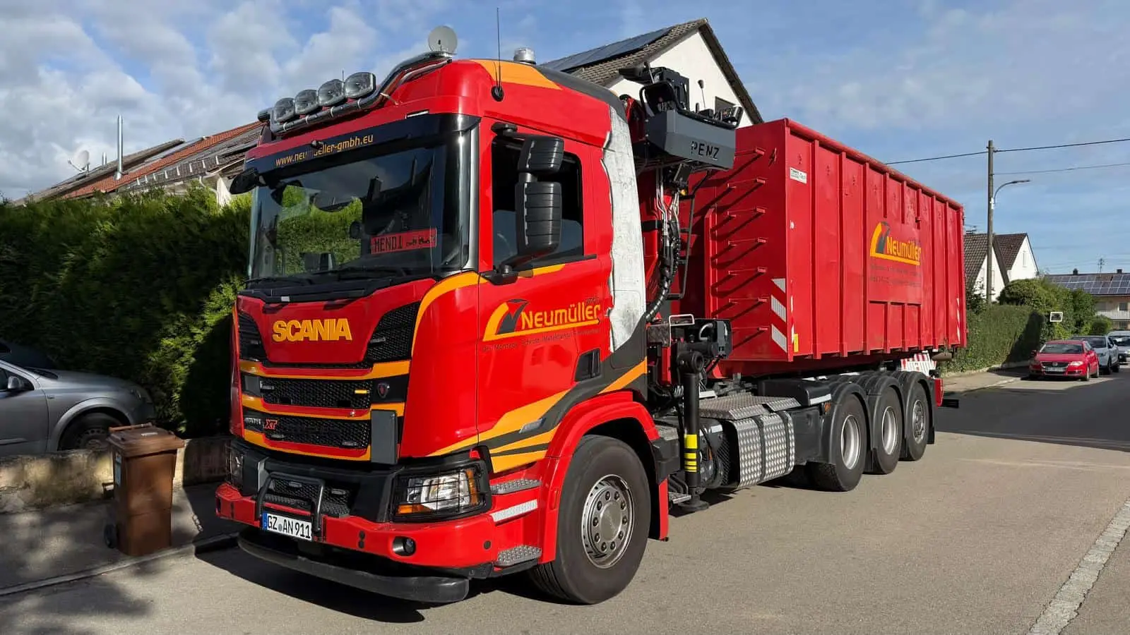 Roter Scania-LKW der Neumüller GmbH mit Ladekran und beschriftetem Abrollcontainer